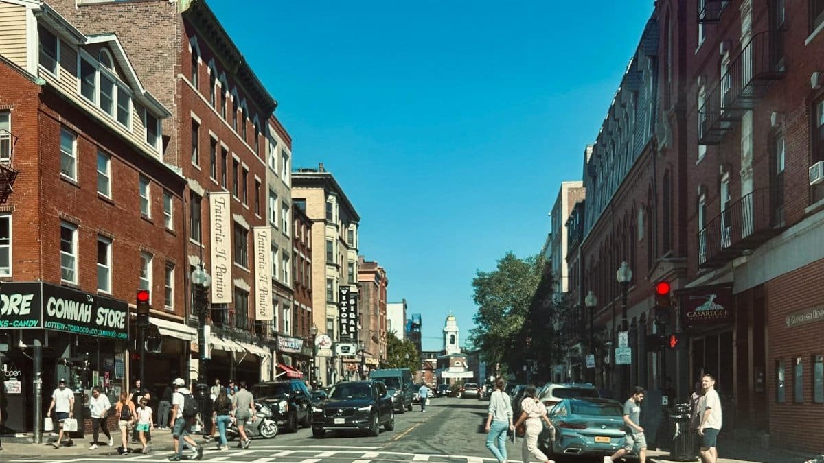 Vibrant street view of Hanover Street in Boston's North End with pedestrians and red brick buildings.