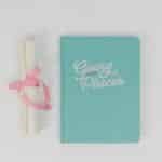 Flat lay of a turquoise notebook with 'Going Places' text and rolled certificate tied with pink ribbon.
