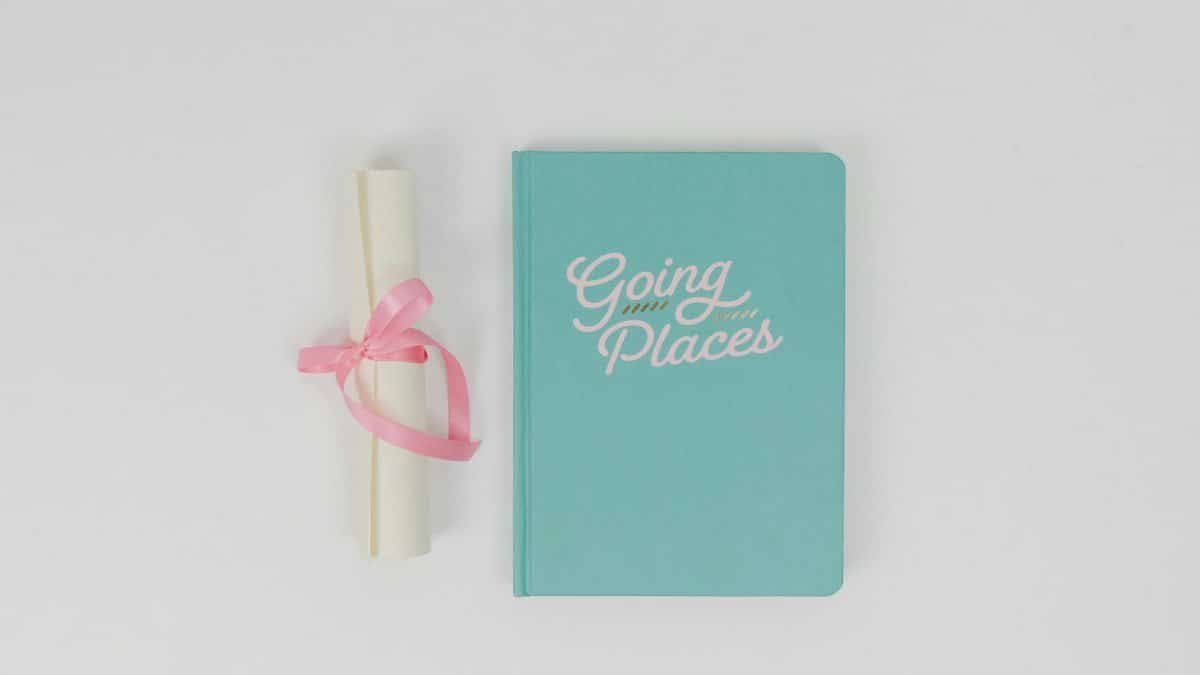 Flat lay of a turquoise notebook with 'Going Places' text and rolled certificate tied with pink ribbon.