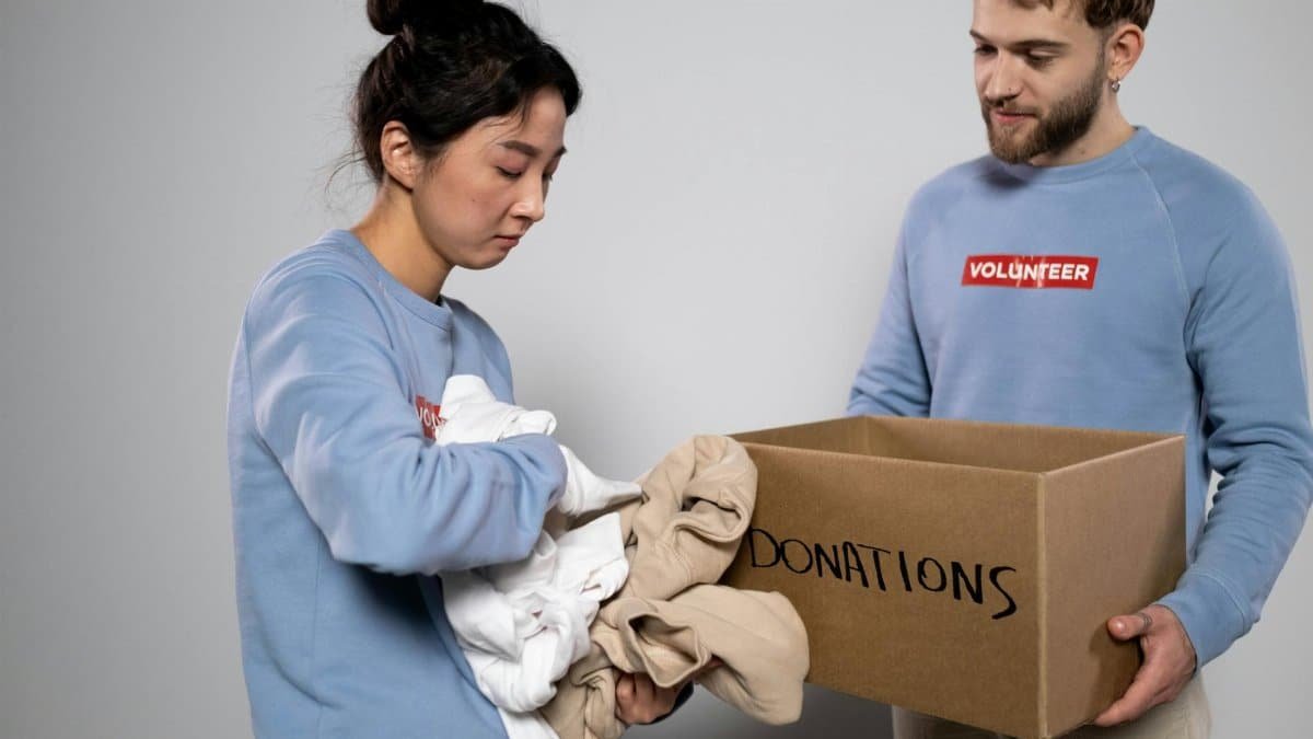 Two volunteers organizing clothes into a donation box, showcasing community service and generosity.