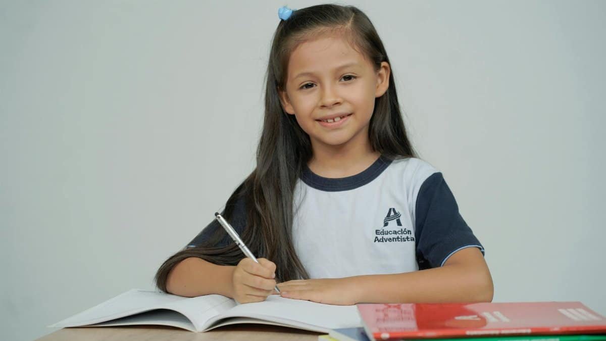 A young girl sitting at a desk, studying with open books and smiling.