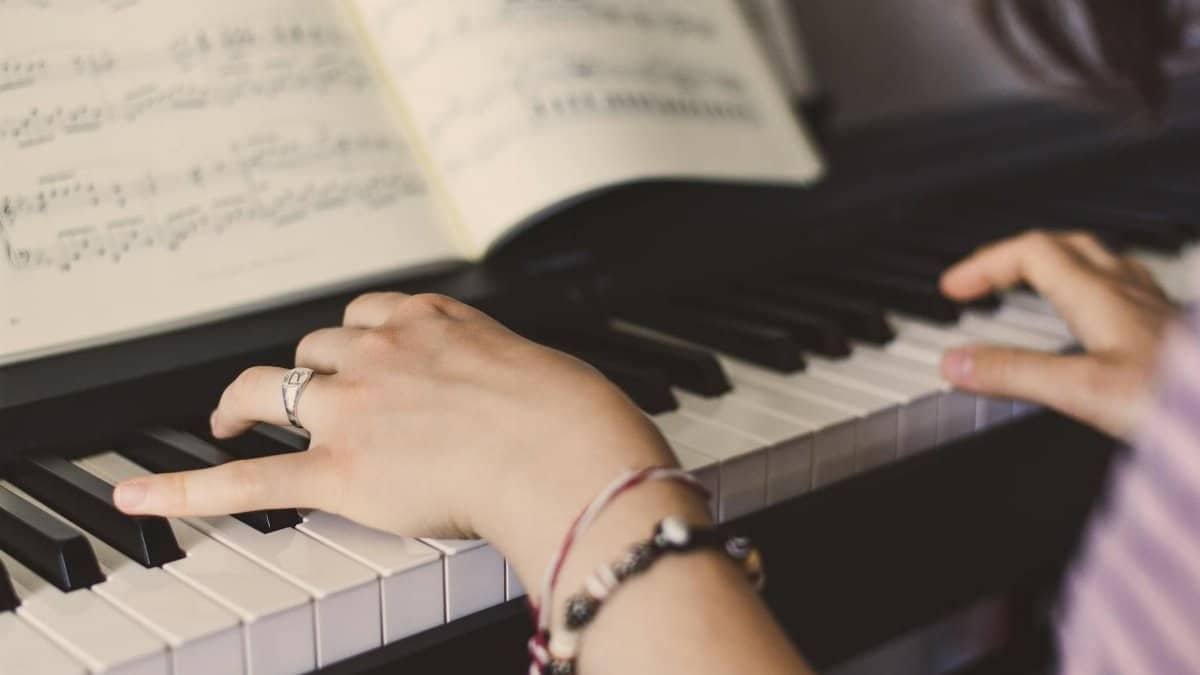 Hands playing piano with sheet music in the background, showcasing musical skill.