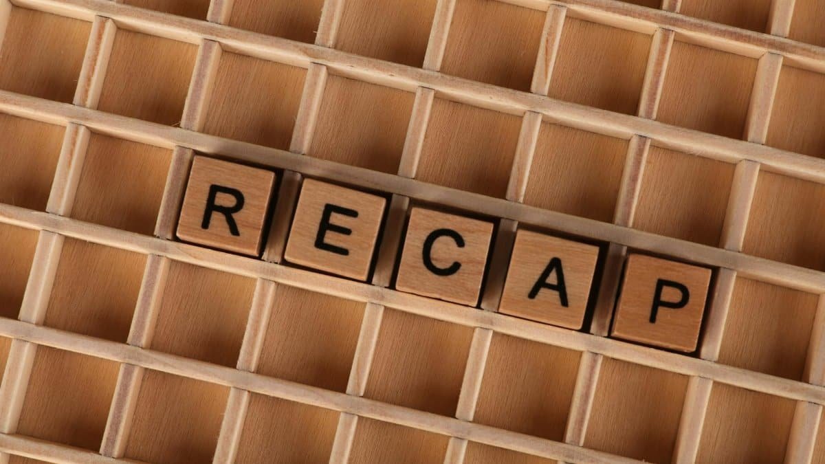 Wooden blocks forming the word 'Recap' on a wooden grid background.