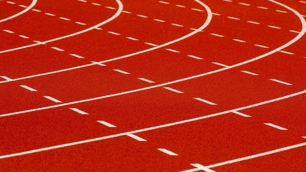 Close-up view of a curved red running track with dashed white lines for athletic sports.
