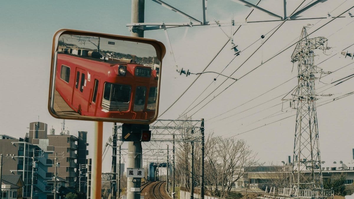 A red train is reflected in a roadside mirror along a railway in Toyota, Japan.