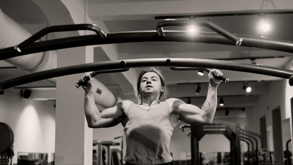 Grayscale image of a man doing pull-ups in a gym, showcasing strength and focus.