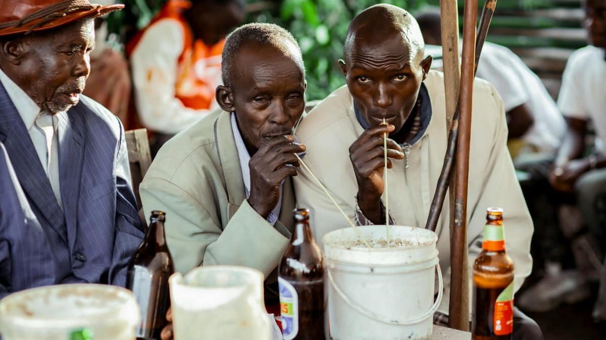 Elderly men enjoying a traditional drink from a bucket outdoors, capturing cultural gathering vibes.