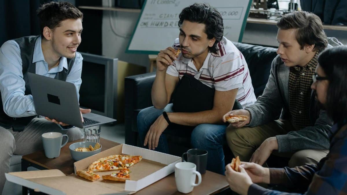 Group of young men having pizza and discussing ideas during a startup meeting in a casual setting.