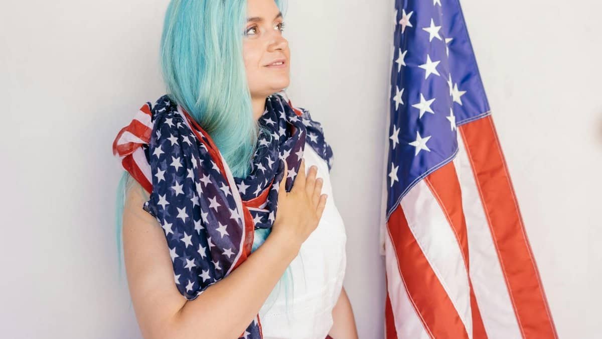 Caucasian woman draped in American flag standing by stars and stripes, showing patriotism.