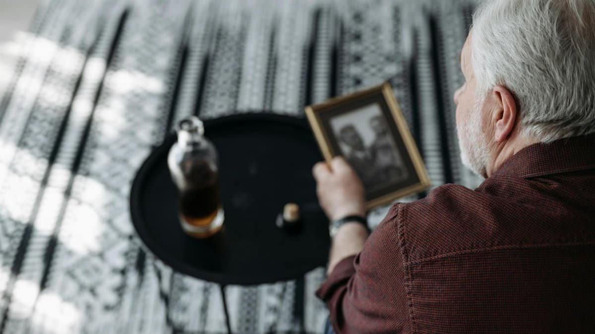 Senior man holding a picture frame, evoking nostalgia and reflection indoors.