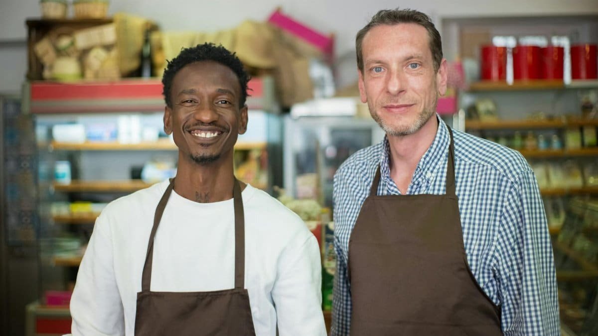 Two happy store owners smiling while wearing aprons in a local grocery store.