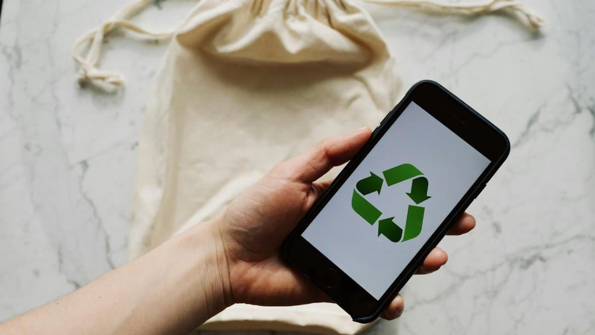 From above view of crop person holding smartphone with recycling symbol on screen and white textile bag placed on marble table