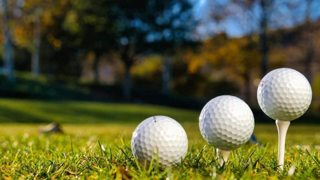 Three golf balls on tees ready for play on a bright sunny day in a green field.