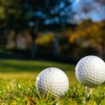 Three golf balls on tees ready for play on a bright sunny day in a green field.