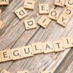 Wooden letter tiles spelling 'Regulation' on a textured wood background, conveying themes of compliance and structure.