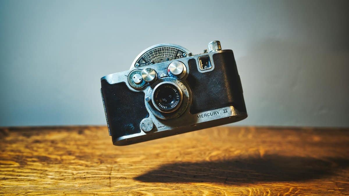 Professional retro photo camera Mercury ll located in air above wooden table against gray background