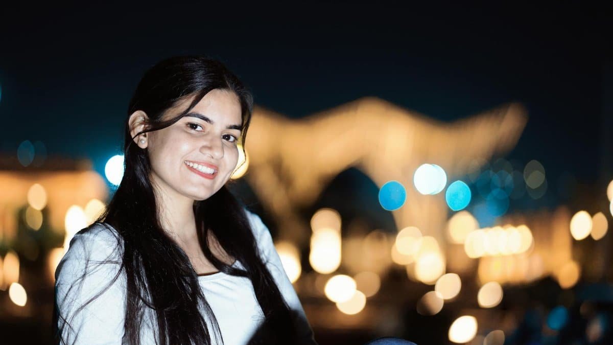 A young woman smiling against a blurry city lights backdrop at night.