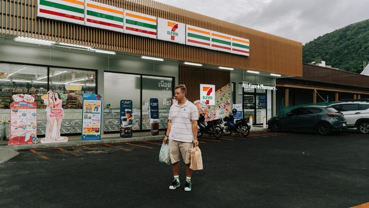 Man with shopping bags outside 7-Eleven in Phuket, showcasing a modern convenience store.