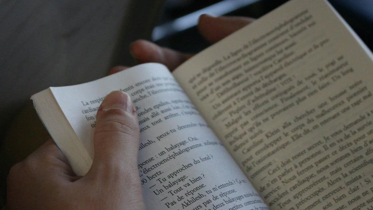 A person reading a book, focusing on the text and hands, in a cozy indoor setting.