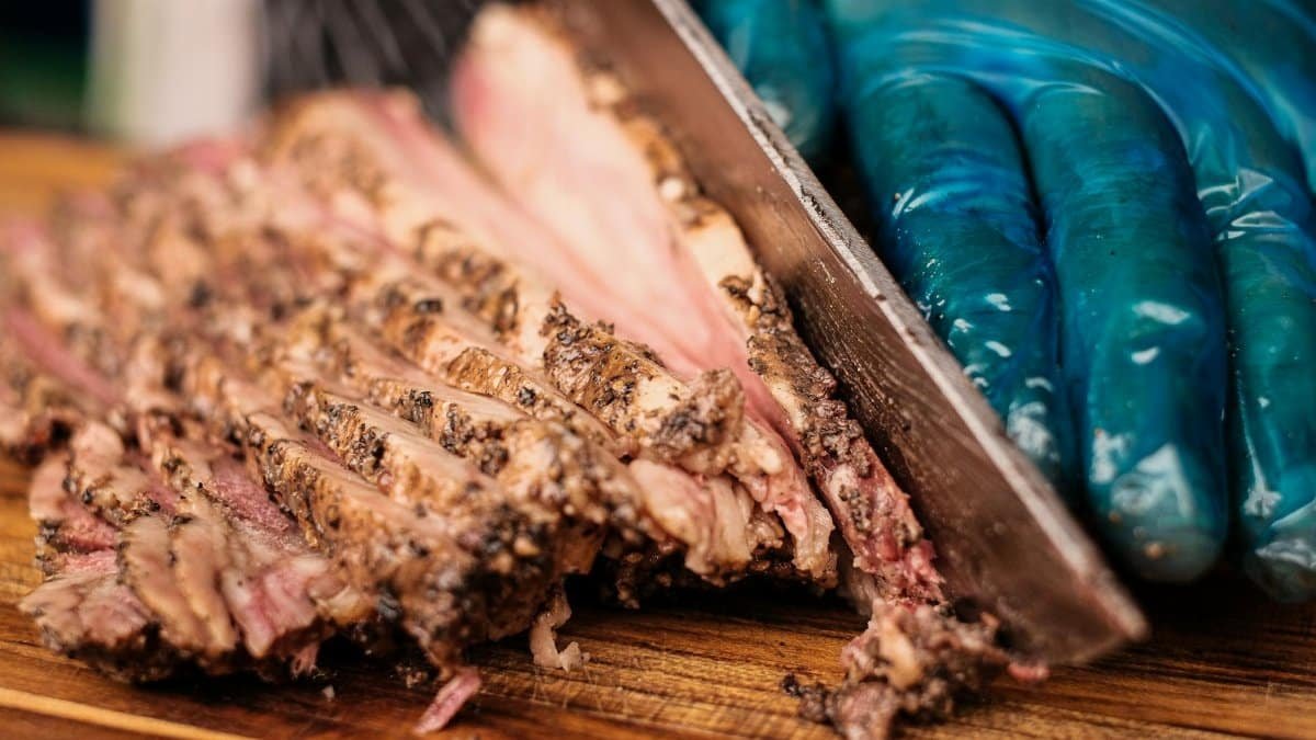 Barbecue brisket being expertly sliced by a gloved hand on a wooden cutting board.