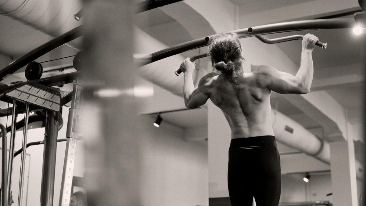 Focused on a man doing pull-ups in a gym, showcasing strength and fitness.