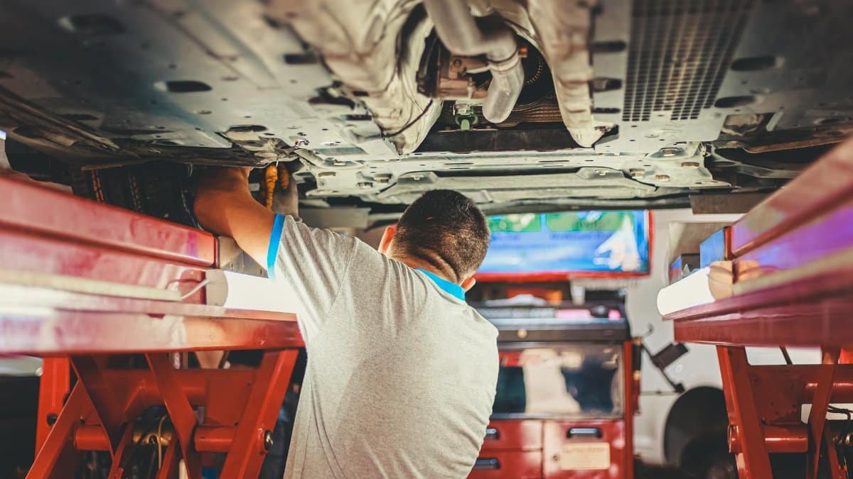 A mechanic works under a lifted car in an auto repair shop, adjusting parts.