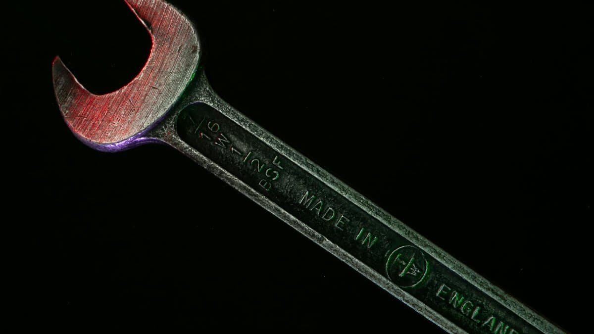 Close-up of a rusty wrench with a red hue on a dark background.