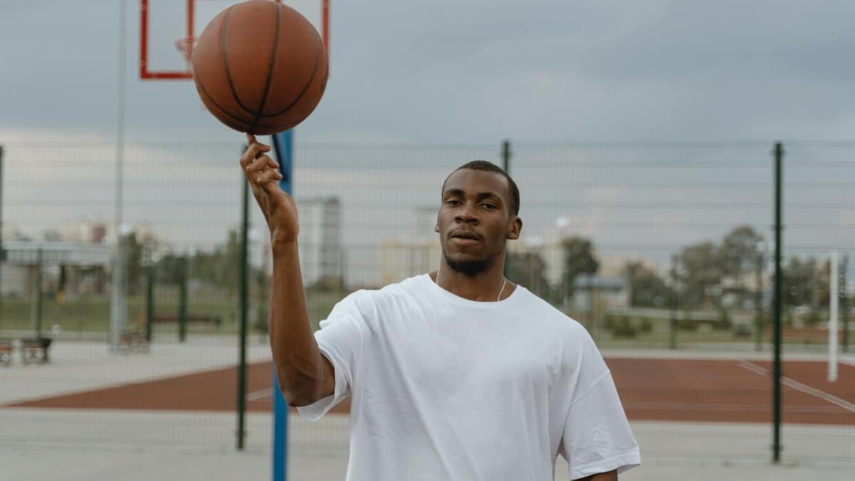 A young black man spins a basketball on his finger on an outdoor court, showcasing sports skills.