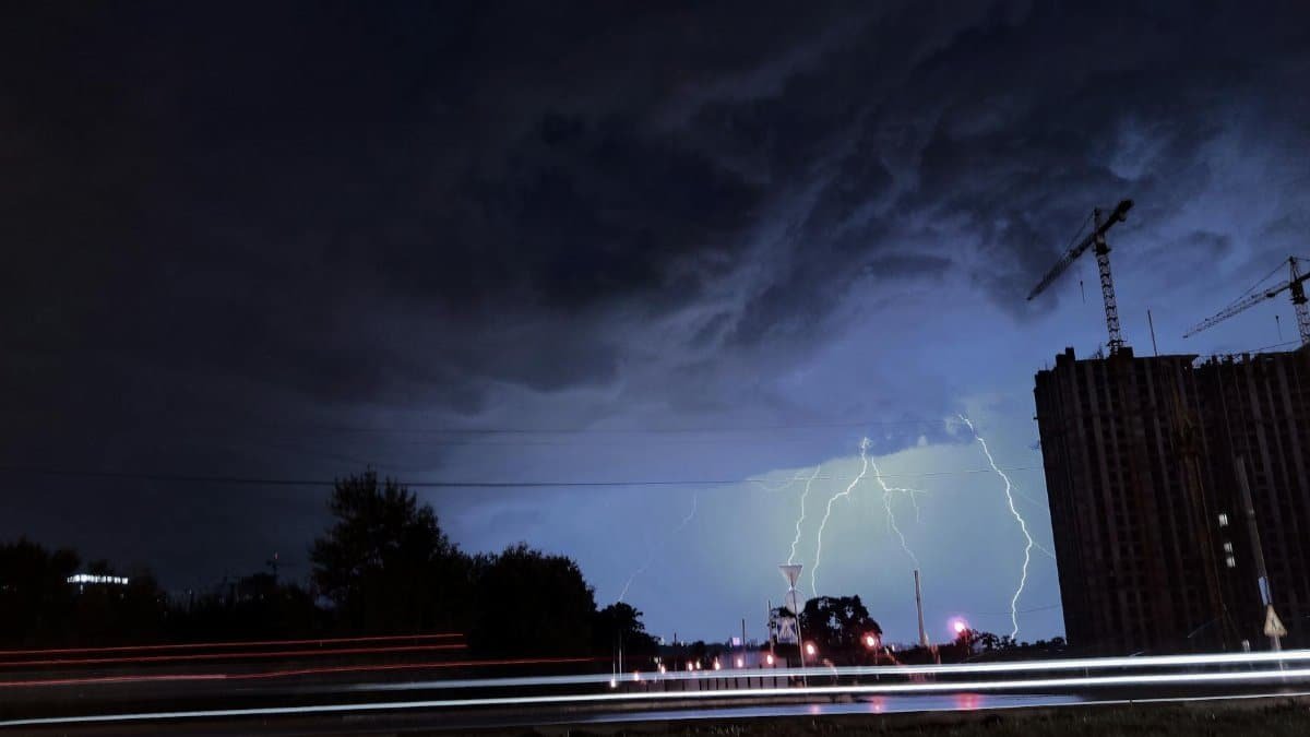 Striking lightning illuminates the night city skyline against a backdrop of dark clouds and urban structures.