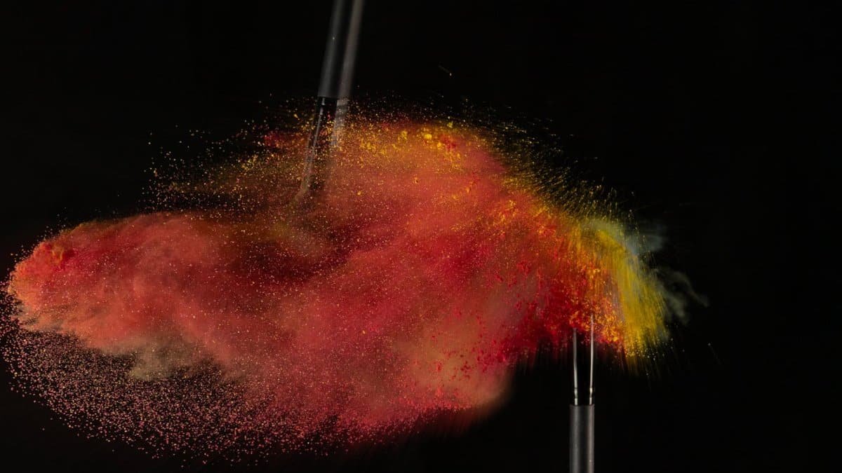 Dynamic photo of vibrant color powder explosion with makeup brushes in motion.