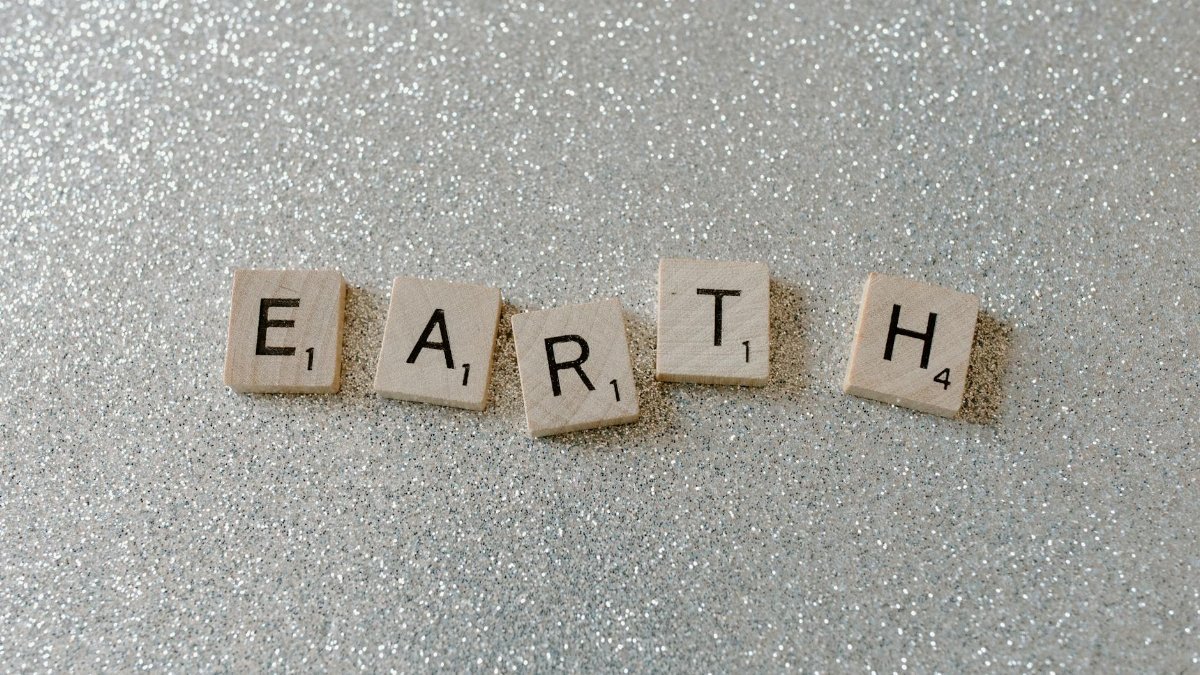 Wooden Scrabble tiles spelling 'EARTH' on a sparkling glitter background.