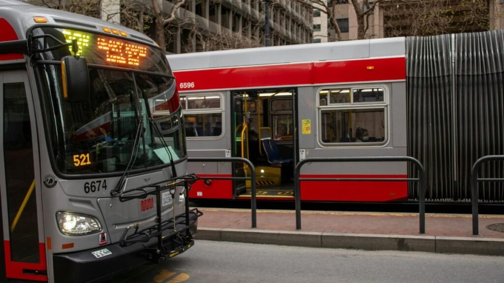 Red and gray buses at a bustling San Francisco downtown bus stop.