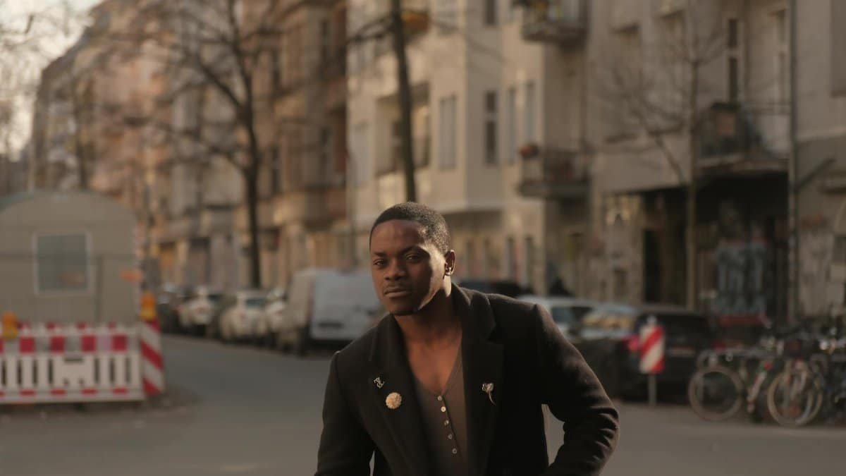 A man in a black coat strolling down a Berlin street, showcasing urban life and fashion.