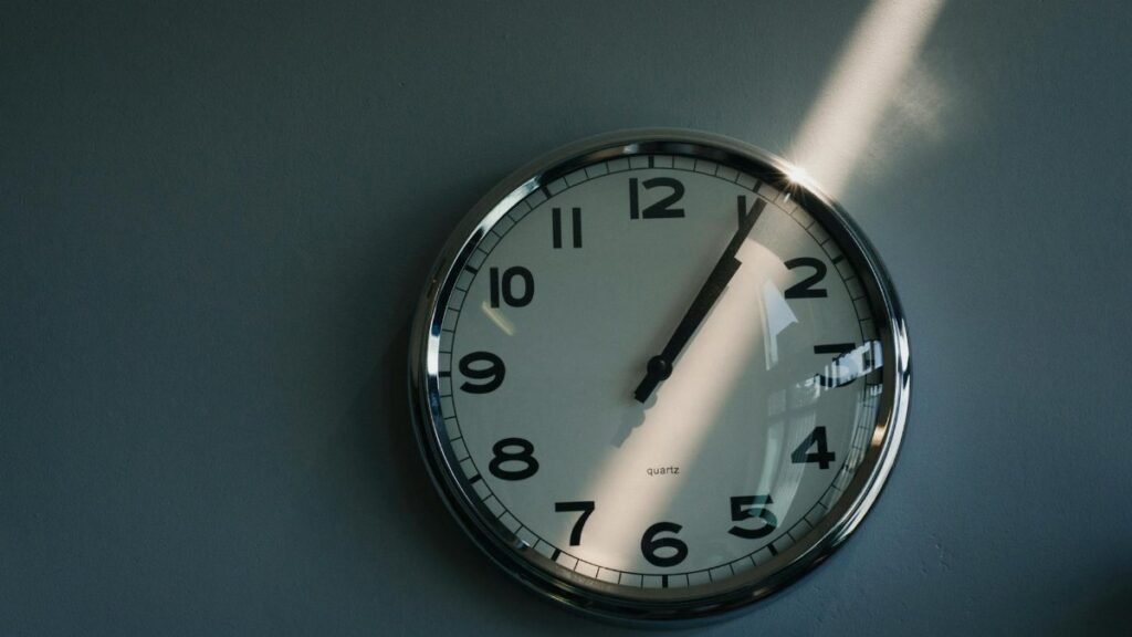 Close-up of a round wall clock illuminated by sunlight indoors, reflecting time passage.