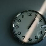 Close-up of a round wall clock illuminated by sunlight indoors, reflecting time passage.