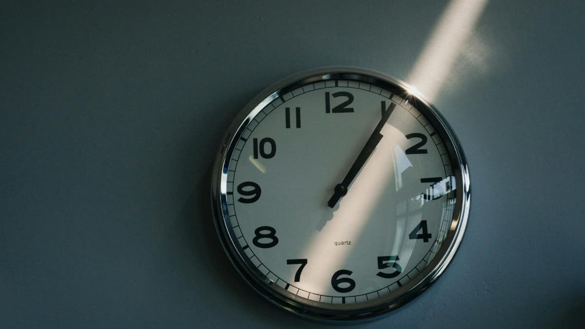 Close-up of a round wall clock illuminated by sunlight indoors, reflecting time passage.