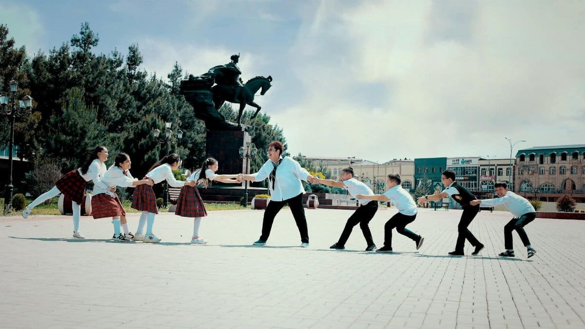 A group of schoolchildren play tug of war by the Babur statue in Navoi Square, Andijan, Uzbekistan.