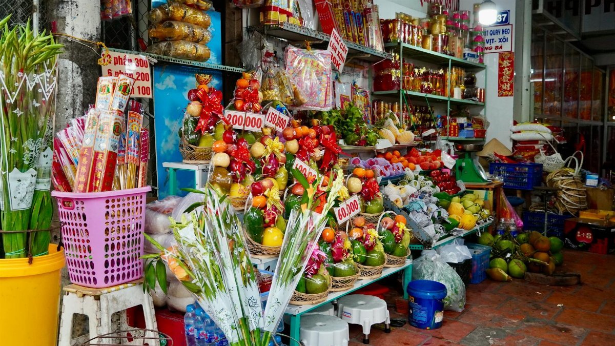 Colorful Vietnamese market stall with fruit arrangements, fresh produce, and cultural items.