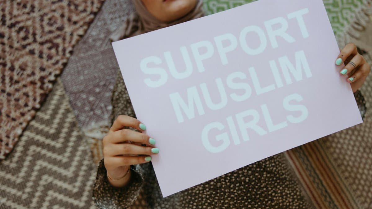 Woman holding a sign with 'Support Muslim Girls' on patterned background.