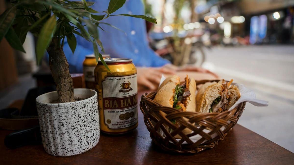 Close-up of Vietnamese banh mi and beer on a Hanoi street-side cafe table, exuding a rustic and authentic vibe.