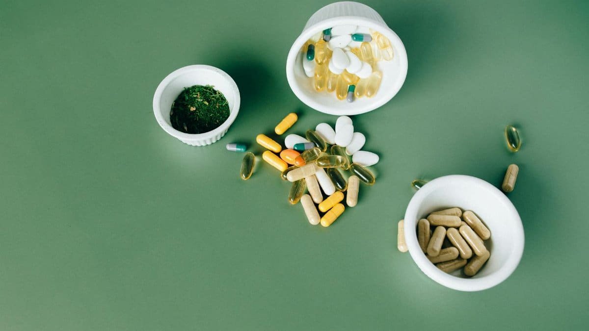 Various herbal and vitamin pills and capsules on a green surface.