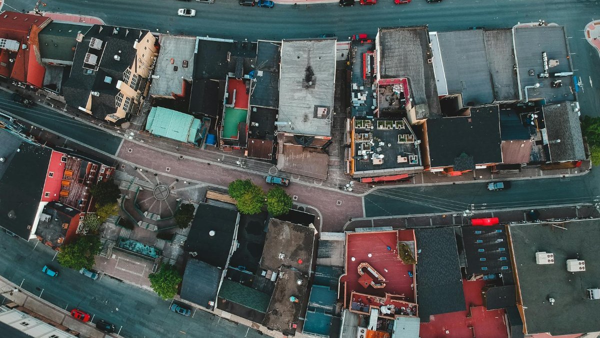 Aerial view of roofs of aged dwelling buildings near asphalt roadways with driving cars in town