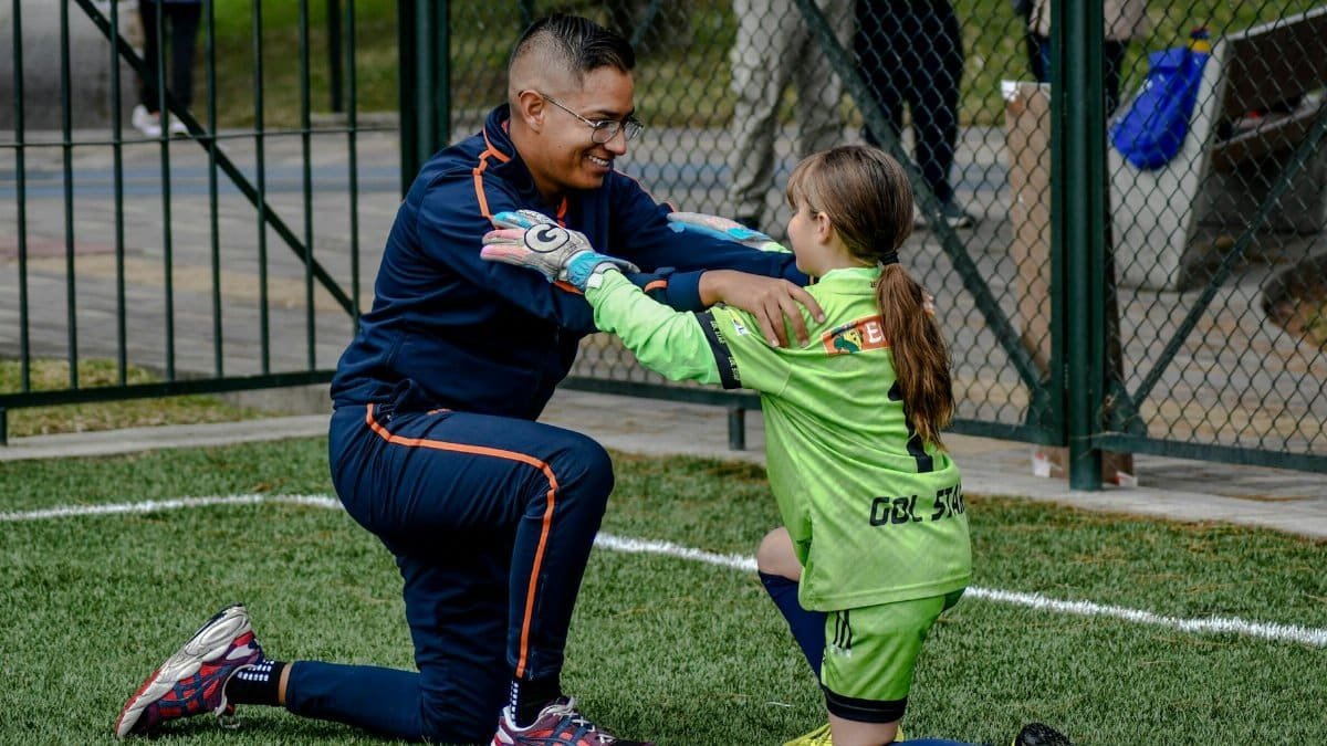 A coach kneels to encourage a young female soccer player in a game.