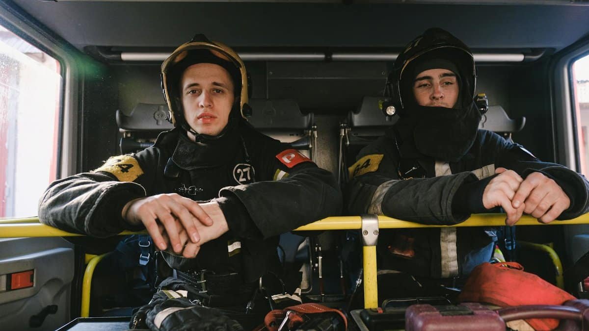 Two firefighters in uniform seated inside a fire truck, ready for action.