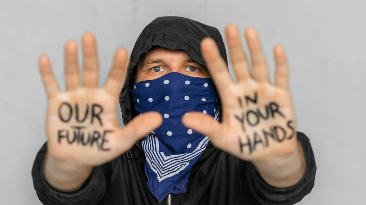 Masked protester displays 'Our future in your hands' for change advocacy.