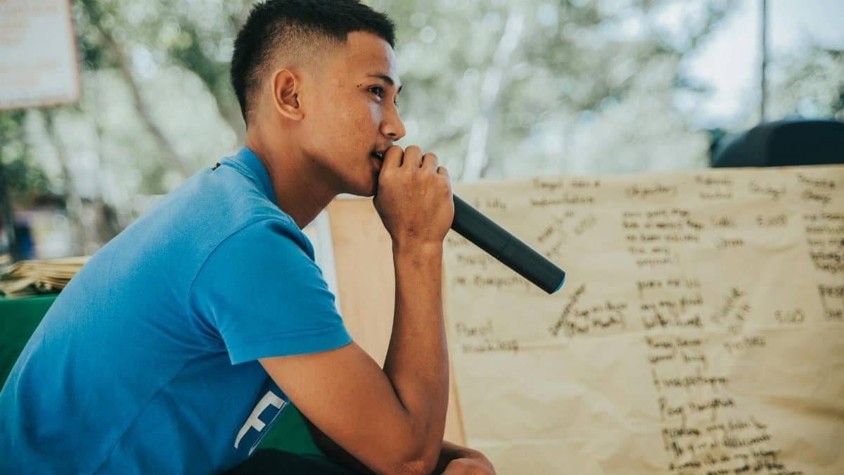 A young man in casual clothing speaks into a microphone outdoors in Calatagan, Philippines.