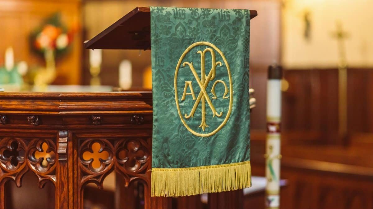 Ornate church altar with green textile and embroidered Alpha Omega symbol in a serene interior.