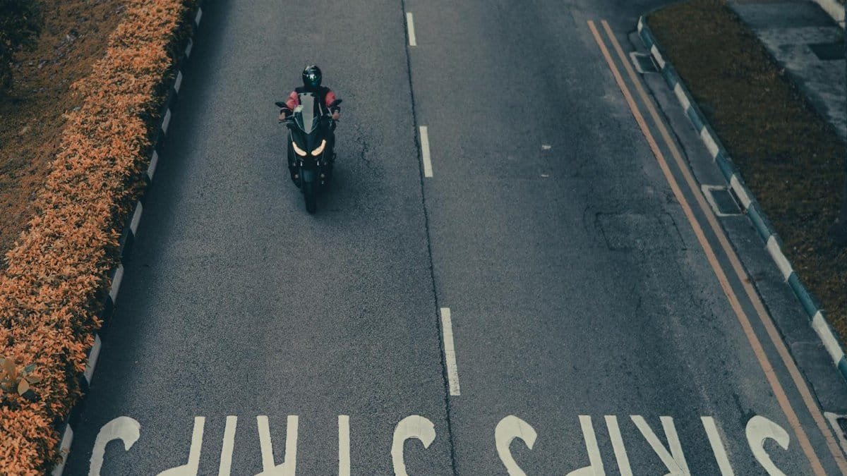 From above of anonymous person in helmet riding motorcycle on empty asphalt road near autumn bushes