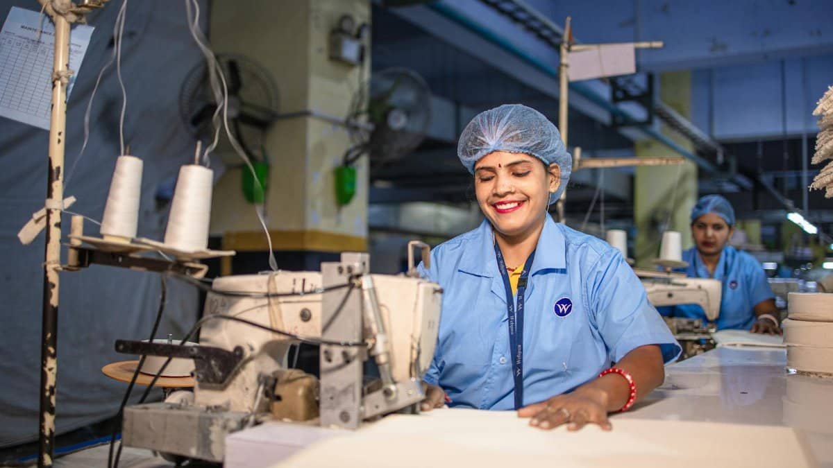 Female textile workers in blue uniforms operating sewing machines in a factory setting.