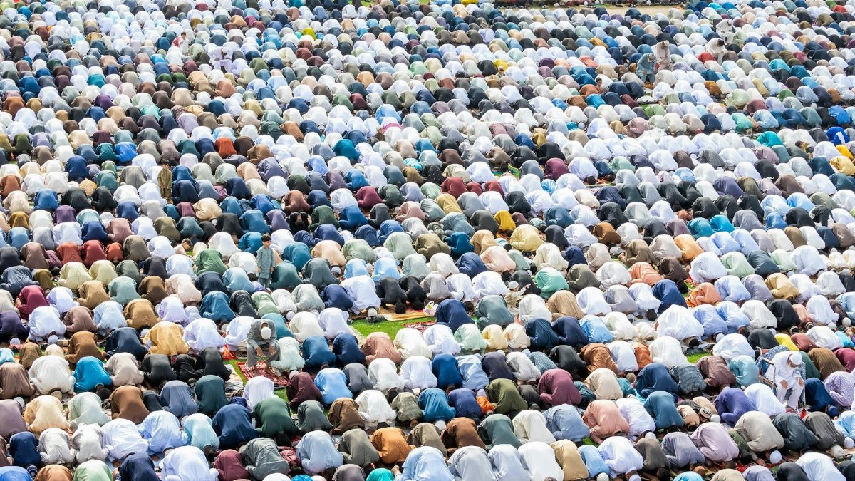 A large crowd of Muslim pilgrims bowing in prayer during an outdoor religious gathering.